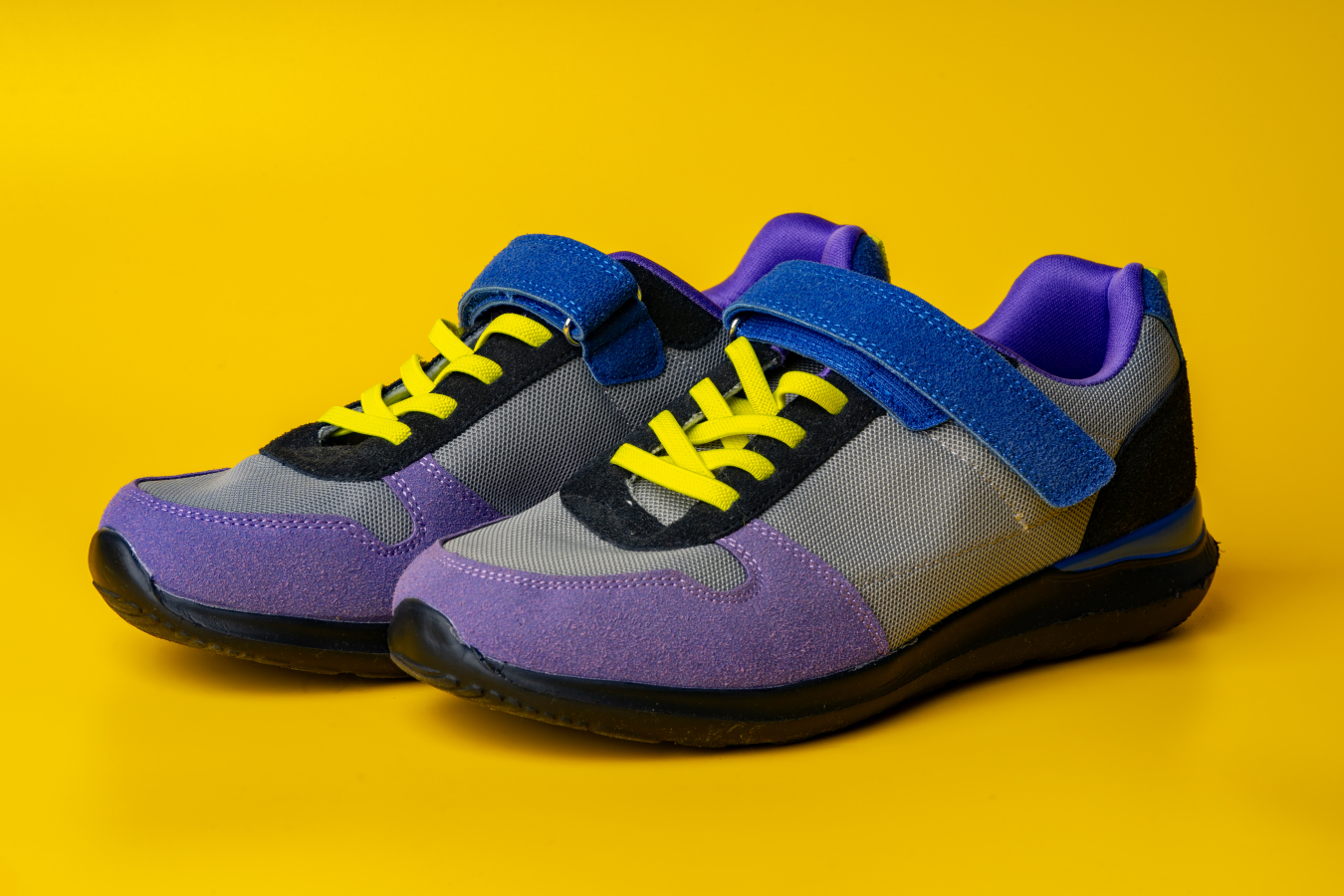 Violet-blue female sneakers on yellow studio background close up