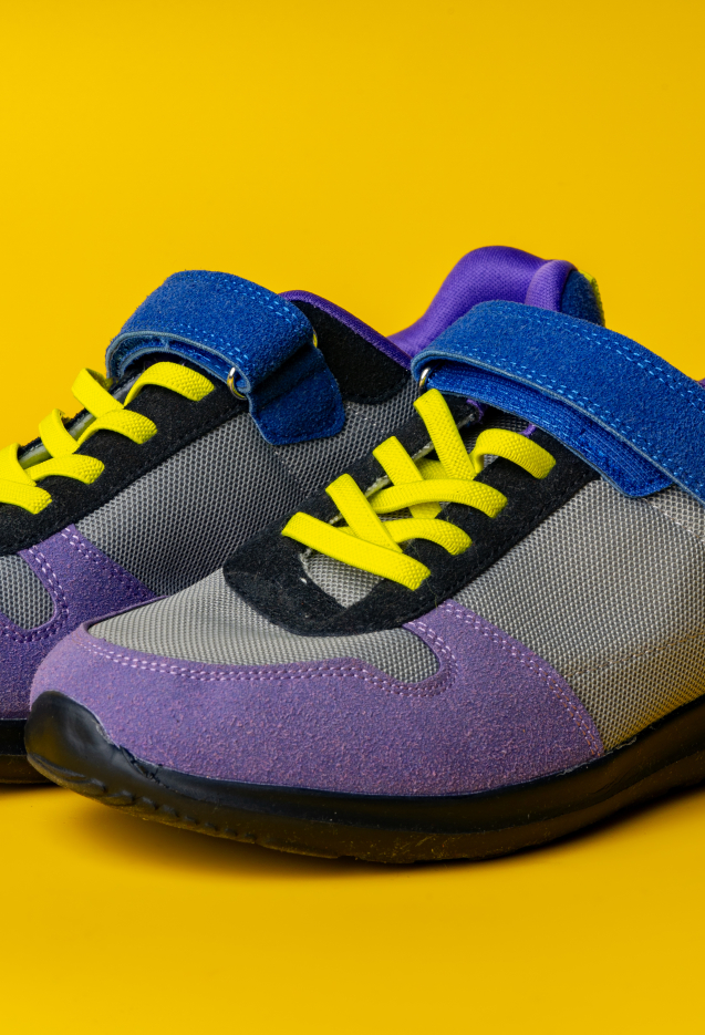 Violet-blue female sneakers on yellow studio background close up